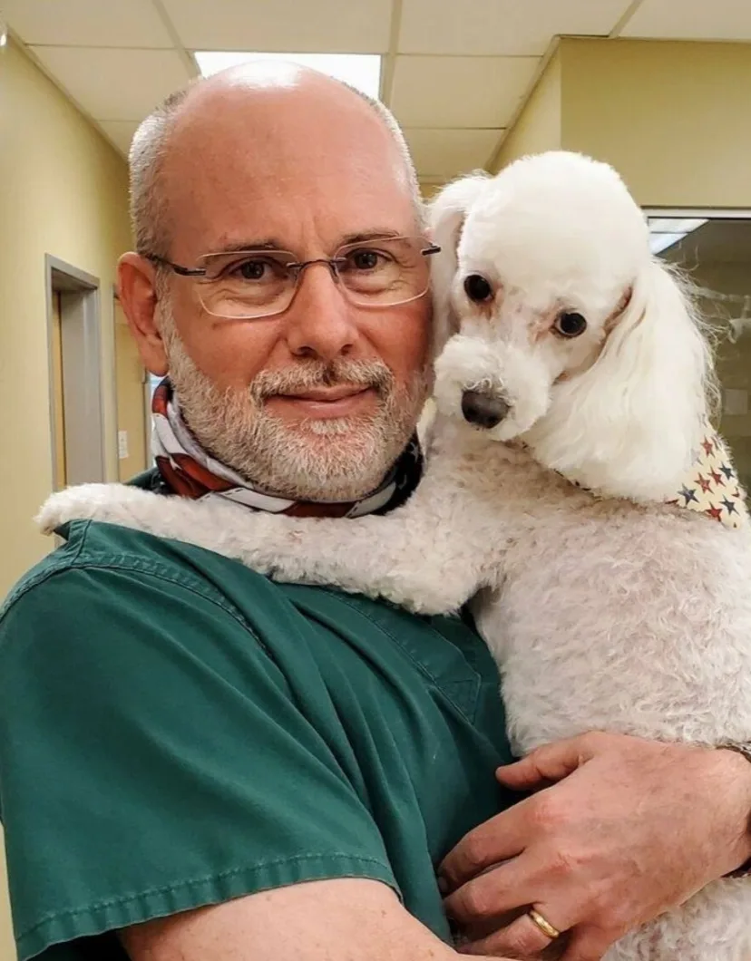 Steven Hibler smiling inside holding a small white poodle.